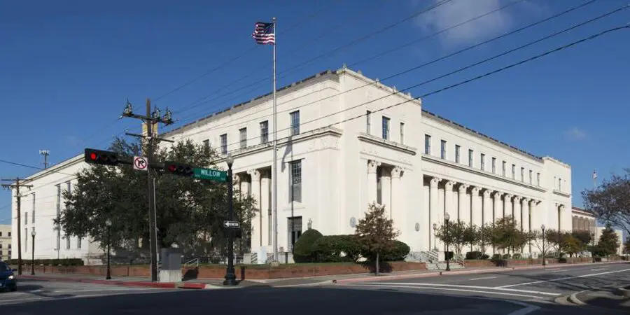 Here's an 8-word alt text for the image: White courthouse with columns under a blue sky.